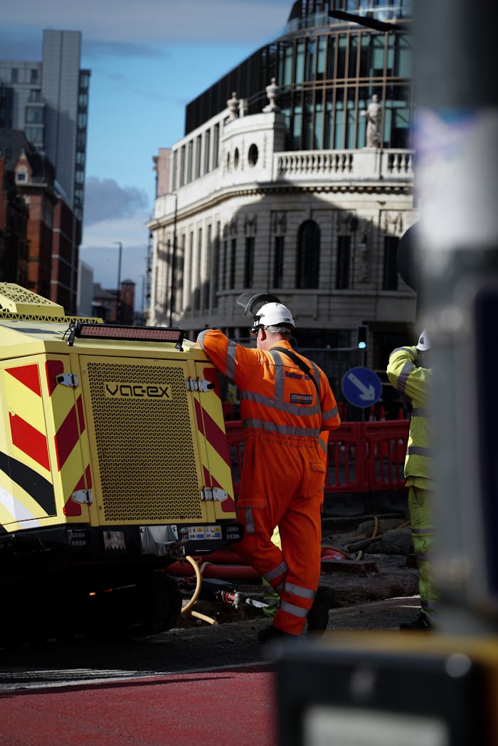 Workers in protective gear manage road construction machinery in a city setting.